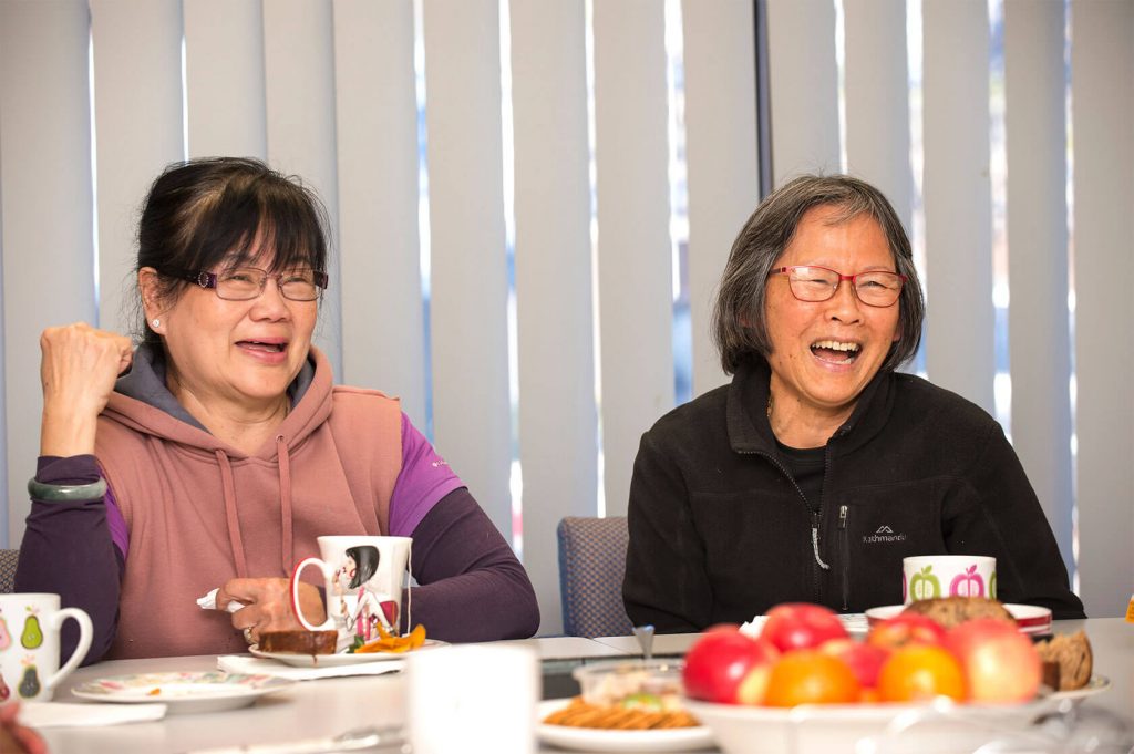 Two migrant women laughing whilst they enjoy morning tea