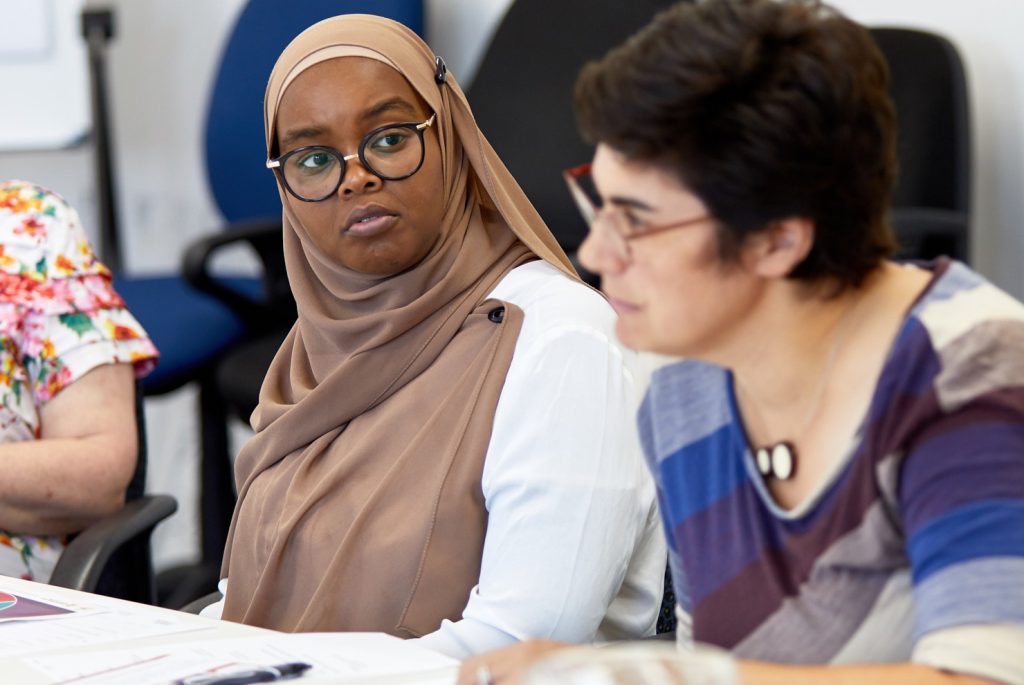 Photo of two ladies at a meeting both wearing glasses and one looking at the other.