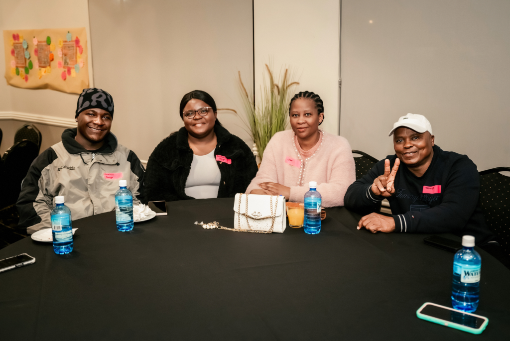 Group of 4 people sitting at a table and smiling, there are two females and 2 males.