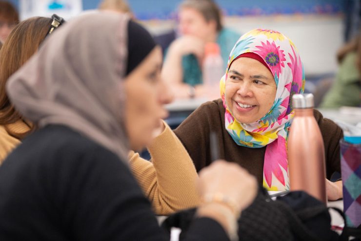 Training group session, with the focus on a migrant woman smiling and wearing a colourful hijab