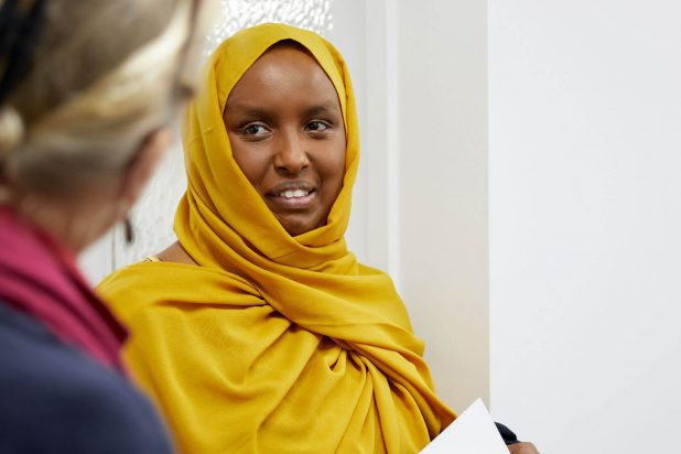 Migrant woman in a yellow hijab talking to another unidentified person